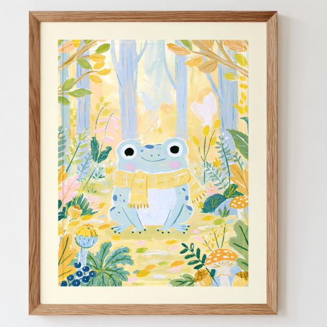 the smiling frog in scarf print in a frame on a wall: A pale blue green frog with big eyes and a yellow striped scarf sits on a golden forest floor framed by leaves, acorns and mushrooms