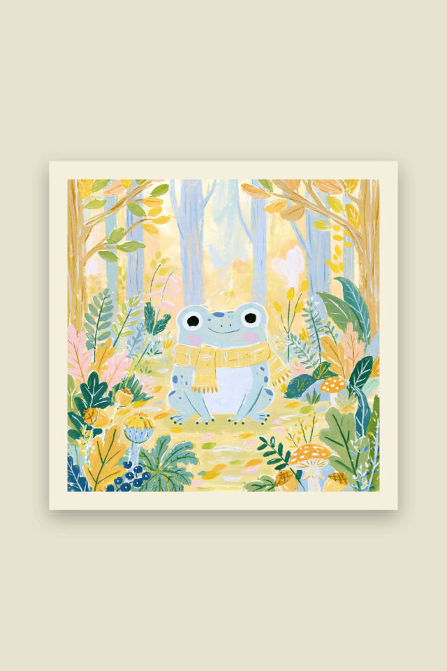 A pale blue green frog with big eyes and a yellow striped scarf sits on a golden forest floor framed by leaves, acorns and mushrooms, on a cream border